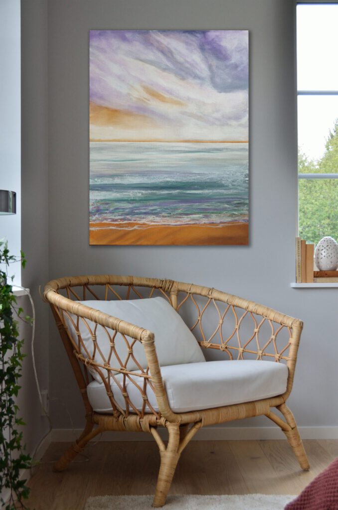 The painting of a beach with an orange sky hangiong in the corner of a grey room.