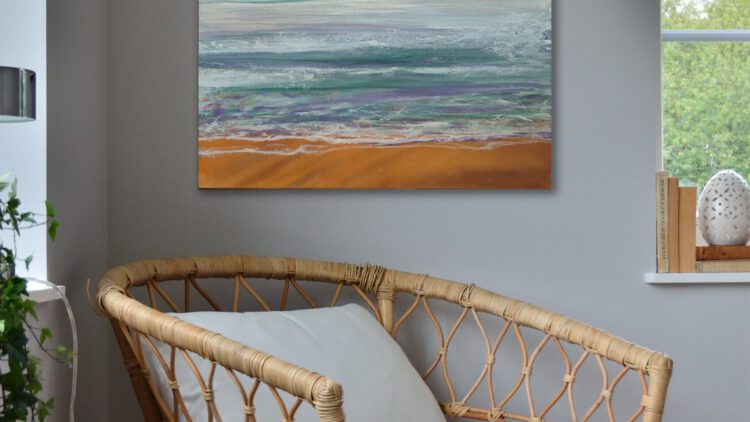 The painting of a beach with an orange sky hangiong in the corner of a grey room.