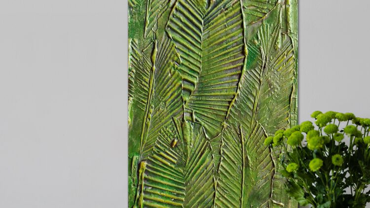 The leaf painting standing on the ground next to a vase of green flowers.