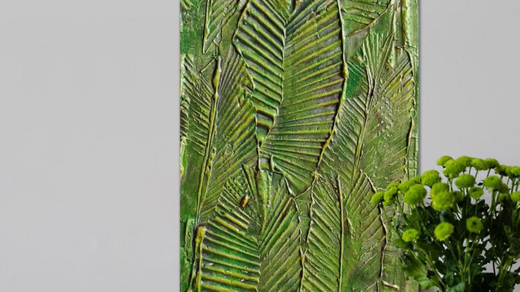 The leaf painting standing on the ground next to a vase of green flowers.