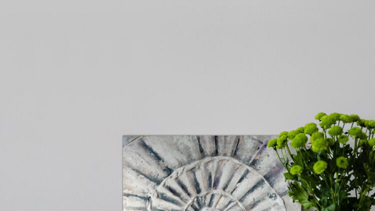 The painting of a shell standing on wooden floor, next to a vase of green flowers.