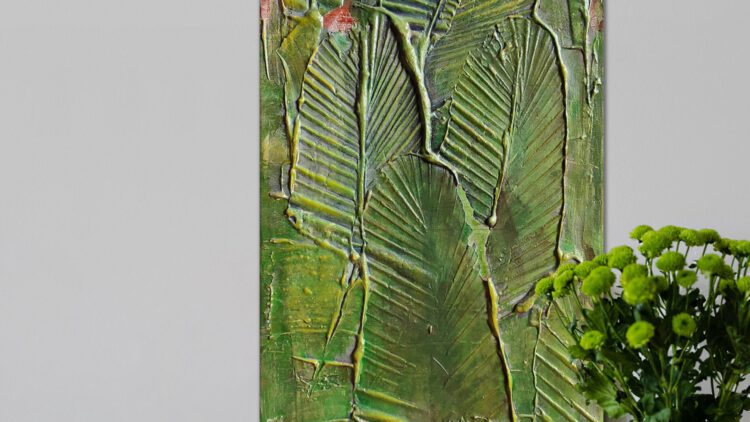 The green leaf painting standing on the wooden floor, next to a flower vase.