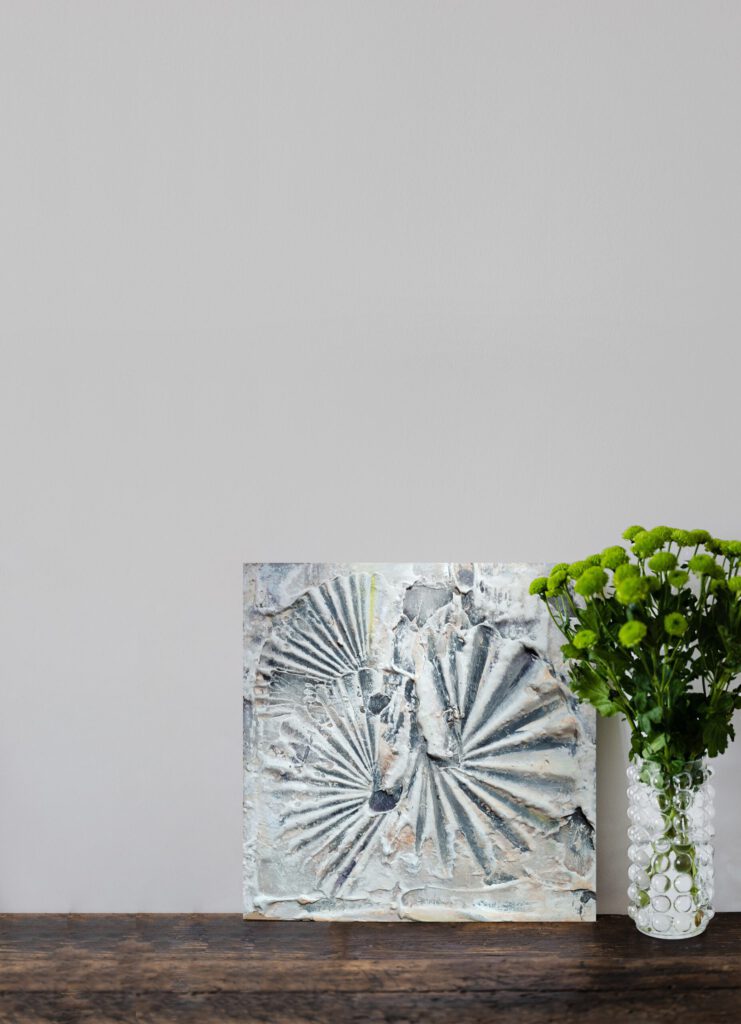 The grey shell painting standing on the wooden floor, next to a flower vase.