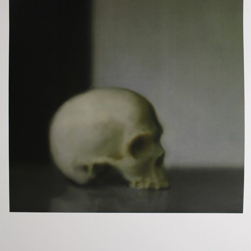 Ein Gemälde eines Schädels ohne Kiefer, der in einer dunklen Ecke steht. Gezeichnet von Gerhard Richter.